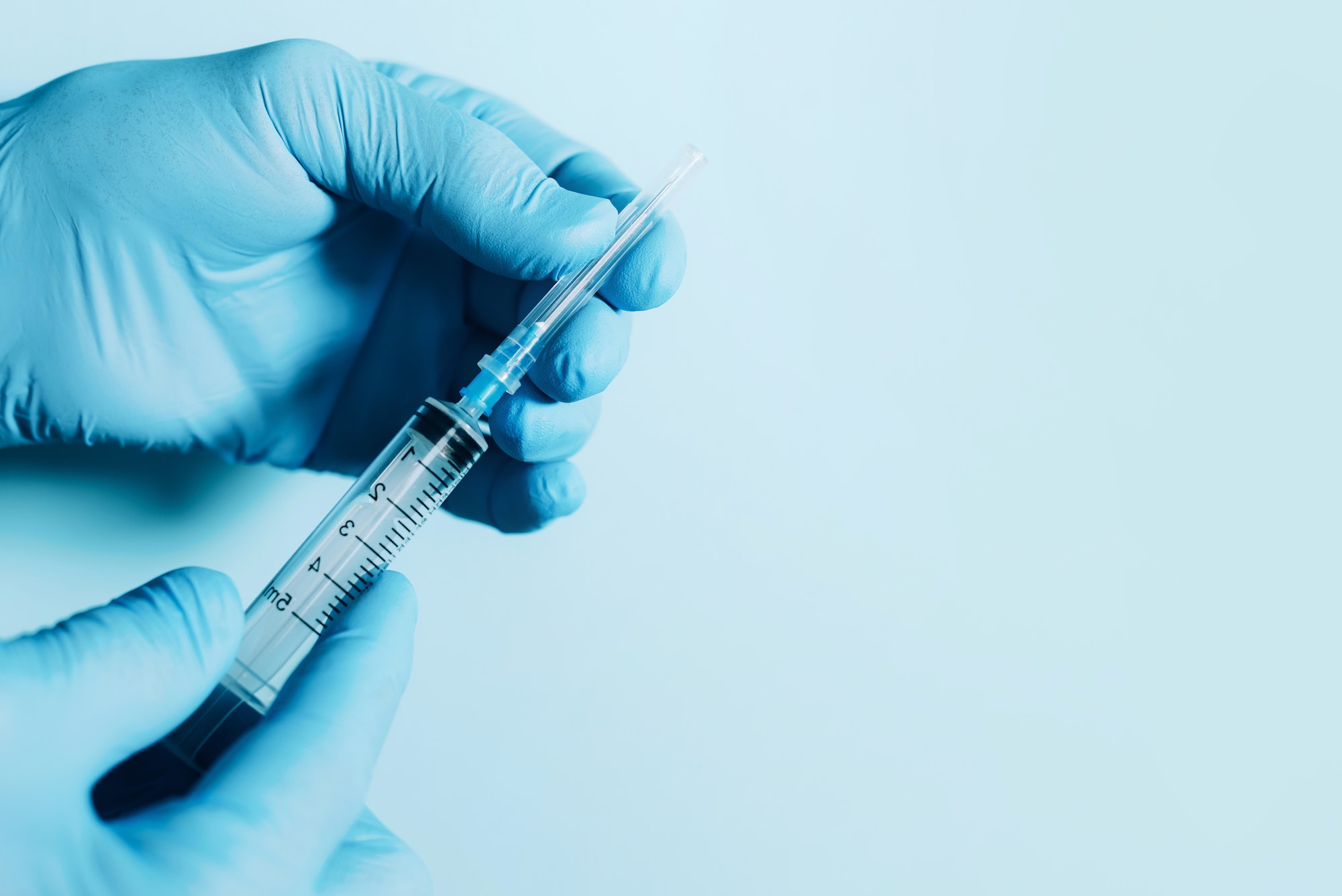 Hand in medical gloves holding syringe on blue background. Copy space. Injections and vaccination